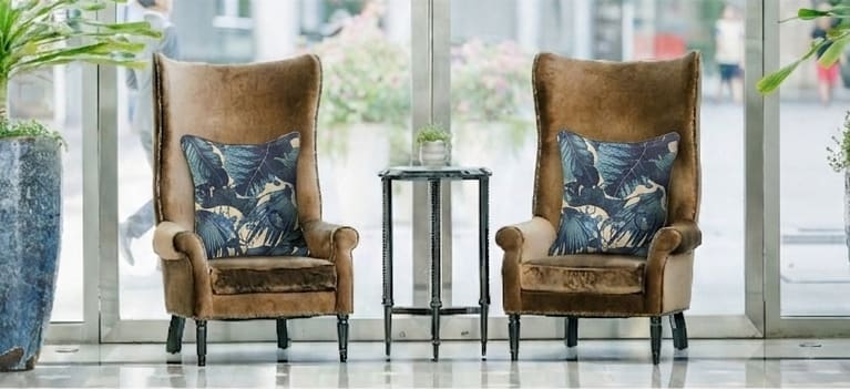 Twee bruine velours oorfauteuils met gebloemde kussens en een ronde bijzettafel