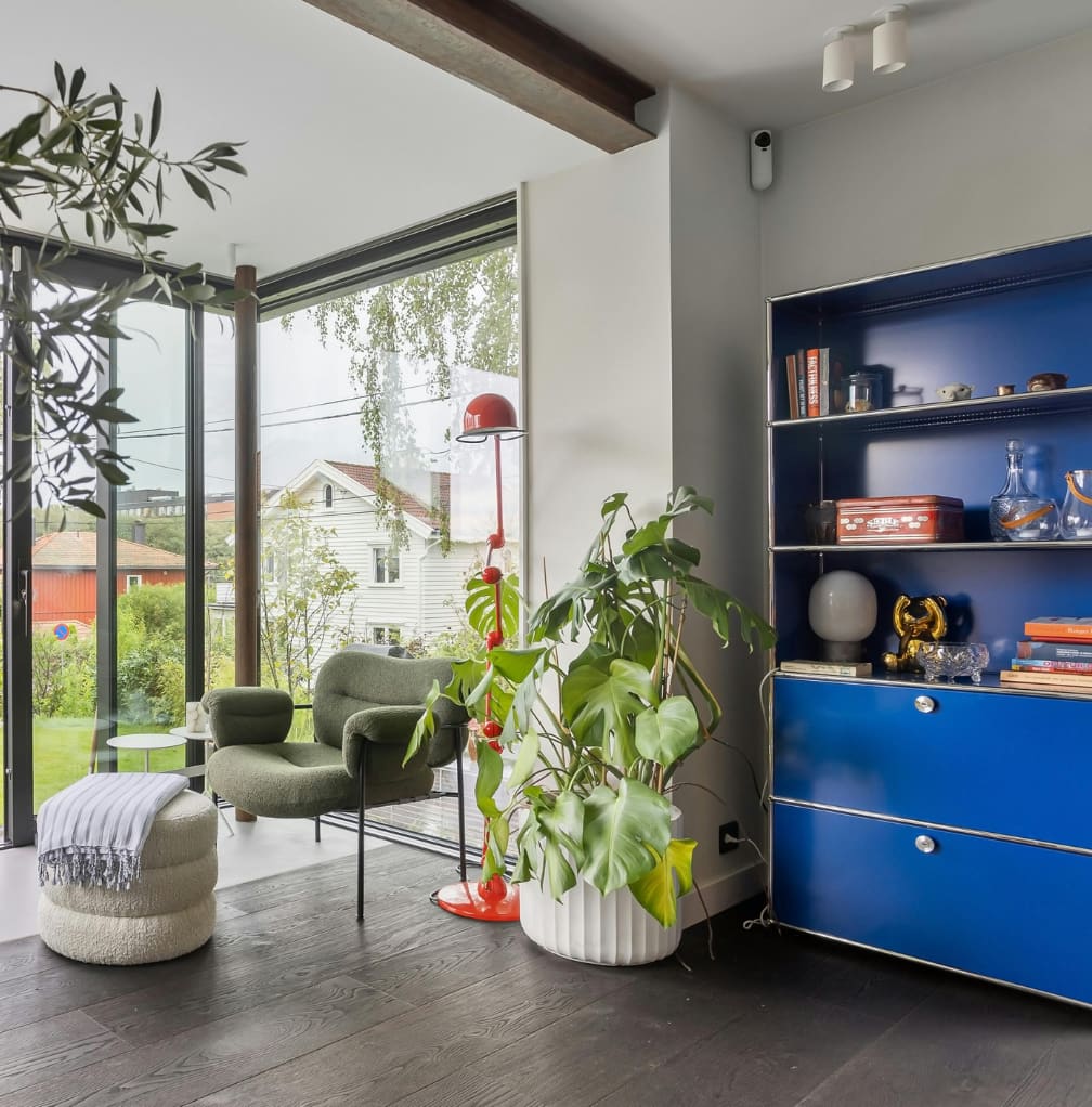 Ontwerp zonder titel (7) (1) Zithoek met groene fauteuils, blauwe kast en veel planten bij een groot raam